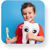 A young boy holding a cushion in the shape of a tooth with eyes in one hand, and a toothbrush in the other.