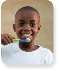 A young boy ready to brush his teeth, holding a toothbrush with toothpaste on it.